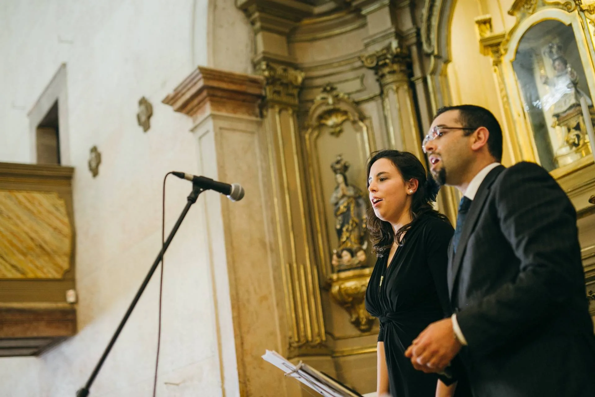 A Joana e o Nelson a atuar num casamento dentro de uma igreja com talha dourada, com um microfone à frente